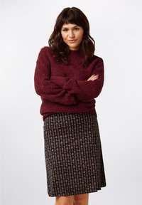 Burgundy tekstiilinjatkona neulepaita pitkillä hihoilla, yhdistettyn�ä kapeaan mustaan hameeseen, jossa on värikäs kukkakuvio.