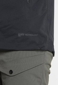 Sorte teknisk jakke med Mammut DRY Technology branding; parret med olivengrønne bukser detaljeret med en sort knap og skræddersyede lommer.