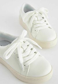 Bílé kožené tenisky s kulatou špičkou, plochými bílými tkaničkami a béžovou gumovou podrážkou. Obsahují švy a texturovanou podšívku.