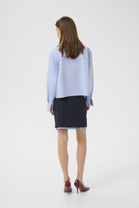 Camicia cropped azzurro chiaro con maniche lunghe, abbinata a una gonna a righe blu navy e tacchi alti bordeaux. Design semplice e sartoriale.