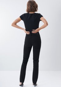 Camiseta negra ajustada y jeans negros de cintura alta. La tela parece suave. Los jeans tienen bolsillos traseros y un ligero estiramiento. Diseño simple.