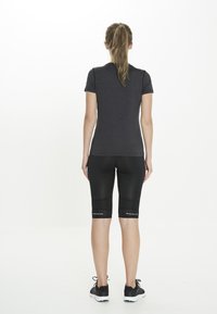 Sort atletisk t-shirt med korte ærmer, kombineret med tætsiddende sorte shorts. Begge dele er lavet af glat, strækbart stof. Sorte sneakers med hvide såler.