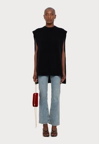 Svart ärmlös stickad topp med raka linjer, i kombination med ljusblå utställda jeans. Modellen håller en liten röd clutch med en gyllene kedja.