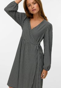 Vestido envolvente de cuadros en blanco y negro con mangas largas abullonadas, escote en V y cinta ajustable en la cintura, hecho de una tela ligera.