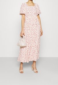 Midi šaty s květinovým vzorem, krátkými nafouknutými rukávy, čtvercovým výstřihem a sukni v několika vrstvách v jemné růžové barvě; doplněné lehkou, nařasenou kabelkou a nahými lodičkami.