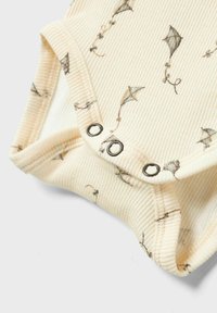 Cremfarbener, gerippter Einteiler mit Drachenmuster. Druckknöpfe am Boden, weicher Stoff. Dezente Farben mit feinen Details im Design.