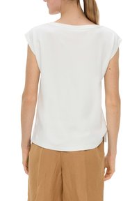 Haut blanc à manches courtes avec une coupe ample, un col rond et des fentes latérales discrètes. Fabriqué en tissu doux, associé à un pantalon beige clair.