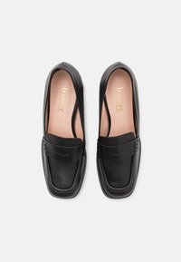 Black leather loafers featuring a smooth texture, rounded toe, and a decorative strap with subtle detailing. Inner lining in beige.