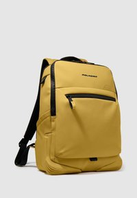 Zaino giallo con finitura liscia opaca, dotato di una tasca frontale nera con cerniera e spallacci neri regolabili. Fondo distintivo texturizzato.