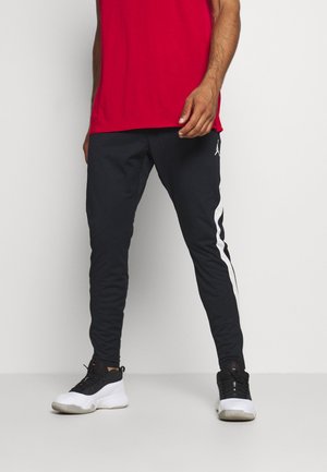 Mustat urheiluhousut, joissa on valkoiset sivusuunnat, kapeat muotoilut ja joustava vyötärö, yhdistettyinä musta-valkoisiin lenkkikenkihin. Punainen paita.