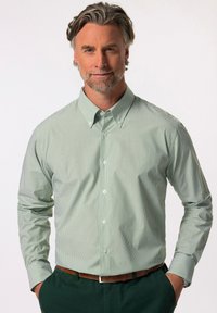 Camicia leggera verde chiaro con sottili strisce verticali bianche, maniche lunghe e colletto a punta, abbinata a una cintura marrone e pantaloni verde scuro.