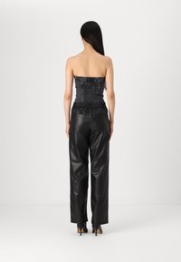 Haut noir sans bretelles avec texture froncée, associé à un pantalon noir en simili cuir taille haute. L'ensemble présente une coupe décontractée et un design minimaliste.