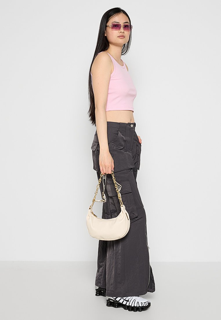 Top corto rosa chiaro, pantaloni cargo grigio scuro con tasche, borsa crema e scarpe bianco e nere con design a righe.