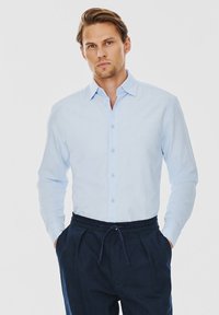 Jasnoniebieska koszula zapinana na guziki, z długimi rękawami, dopasowana, wykonana z mieszanki bawełny. Zestawiona z granatowymi spodniami na sznurku. Minimalistyczny design, gładka tekstura.