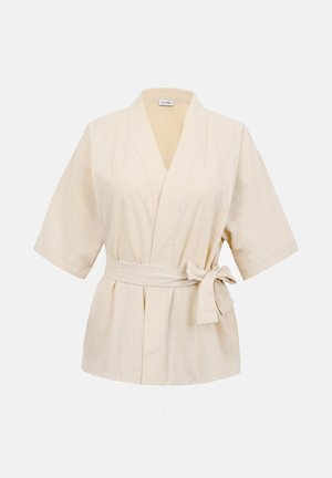 Beżowa krótka bluzka kopertowa z krótkim rękawem, dekoltem w serek, materiałowym paskiem związanym w kokardę w talii oraz luźnym krojem.