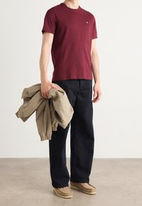 Hnědá krátkotrvající tričko, volné námořnické kalhoty, drží khaki bundu. Doplňky zahrnují prsteny a béžové slip-on boty.