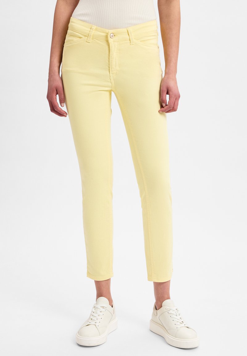 Gelbe eng geschnittene Jeans mit glatter Oberfläche, mittlerer Taille und Fünf-Taschen-Design, kombiniert mit weißen Sneakers.
