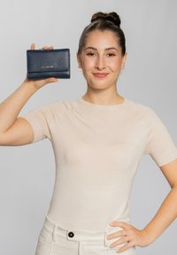 Billetera de piel azul marino con acabado texturizado, que presenta un cierre de solapa y el logo de la marca, sostenida por una persona contra un fondo neutro.