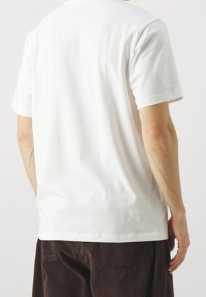 Homme portant un t-shirt blanc uni à manches courtes et un pantalon en velours côtelé marron foncé, vu de dos.