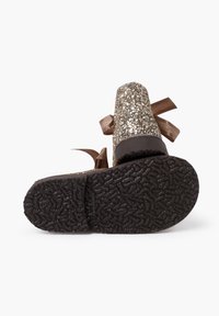 Zapatos de plataforma dorados brillantes con una superficie lisa, punta redondeada y lazos de satén marrón en la parte trasera; suela de goma negra texturizada.