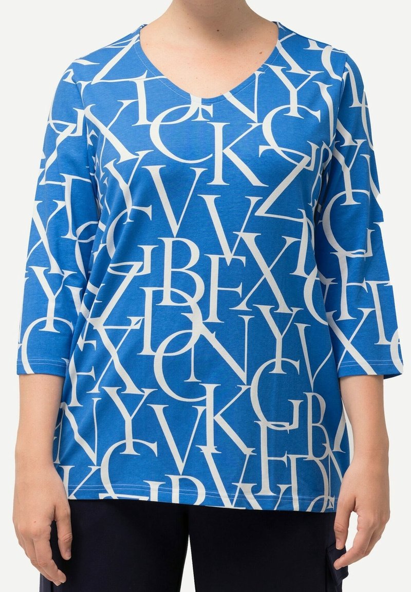 Blauer Baumwolloberteil mit 3/4-Ärmeln, das ein großes weißes Alphabet-Muster aufweist. V-Ausschnitt-Design mit lockerer Passform.