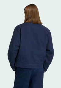 Tmavě modrá bomber bunda s uvolněným střihem, vyrobená z hladké bavlněné tkaniny. Obsahuje patentku na lemu a minimální detaily šití.