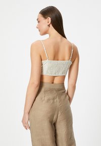Lysfarvet cropped top med et ternet mønster og smocket tekstur. Kombineret med højtaljede, strukturerede beige bukser.