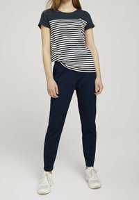 Navy raidallinen t-paita lyhyillä hihoilla ja kaarevalla helmalla, yhdistettynä tummansinisiin slim-fit-housuihin. Vaaleat lenkkarit viimeistelevät asun.