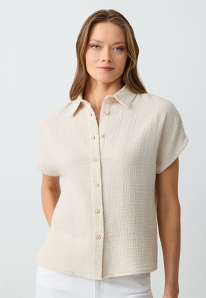 Lichtbeige overhemd met knoopsluiting, gemaakt van textuurstof, met een kraag, korte mouwen en zeven kleine knopen aan de voorkant.