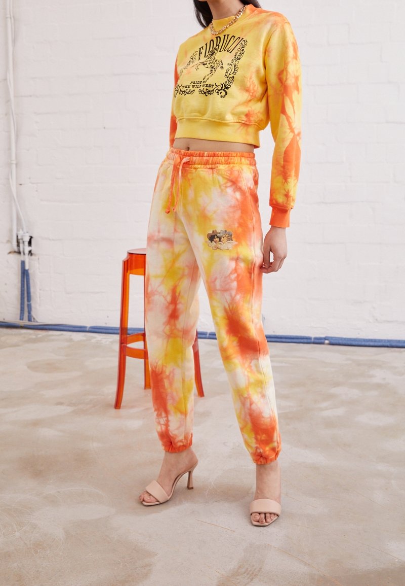 Geel-oranje tie-dye cropped sweatshirt met zwarte tekst, gecombineerd met bijpassende tie-dye sweatpants met een graphic op het been.