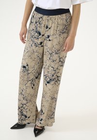 Wide-leg trousers in beige with a dark blue marbled pattern. Features an elasticized navy waistband and a soft fabric texture.