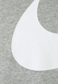 Grått tyg med en slät textur pryds av en stor vit böjd design. Kompositionen innehåller två tydliga färgområden som framhäver kontrasten.