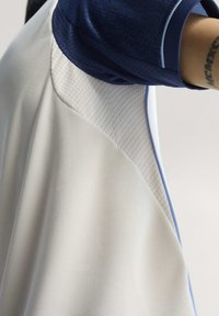Maillot de sport léger avec un haut bleu marine en tissu texturé, un corps blanc à finition lisse, et des coutures accentuées en bleu.