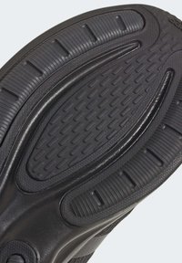 Suola di scarpa in gomma nera con motivi testurizzati, creste e scanalature per una migliore aderenza e flessibilità, con una sezione centrale liscia.