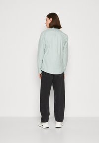 Camicia a maniche lunghe verde menta chiaro con vestibilità rilassata, polsini abbottonati e yoke posteriore, abbinata a pantaloni larghi scuri e sneakers bianche.