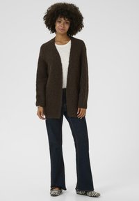 Brown knitted cardigan with a V-neck design, open front, and long sleeves. Paired with dark flared jeans and black-and-white striped shoes.
