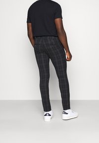 Slim-fit rutiga byxor i mörka nyanser med en subtil textur, med bakfickor och kombinerat med vita sneakers.