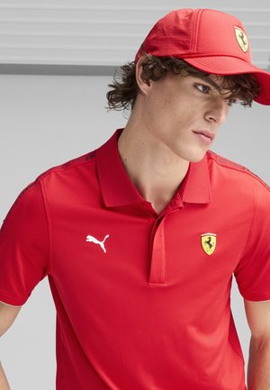 Camisa polo roja con cuello, que presenta un logo de Ferrari y un logo de Puma en blanco. Acompañada de una gorra roja a juego con perforaciones.