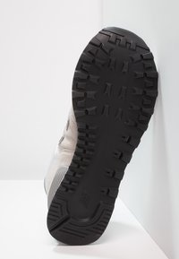 Tossu huulipohja, jossa on kova musta kumitettava pinta, jonka syvät urat tarjoavat pitoa, ja vaaleanharmaa aniliinivanho.]