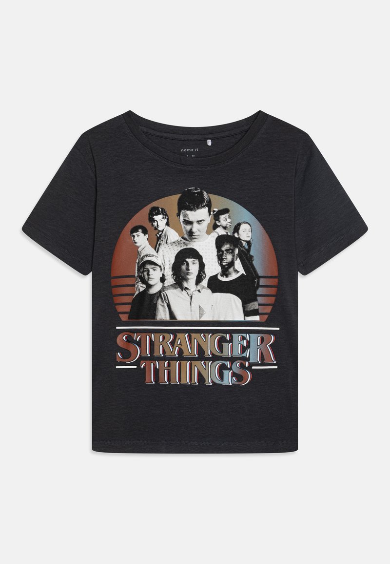 T-shirt graphique noir avec un imprimé circulaire représentant des personnages de "Stranger Things" et le titre en texte audacieux et coloré en bas.