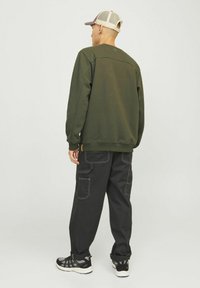 Olivgrüner Crewneck-Pullover und schwarze Cargo-Hosen mit weißen Nähdetails. Schwarze Sportschuhe mit strukturiertem Sohle und Mesh-Akzenten.