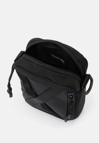 Borsa a tracolla nera con un esterno liscio, apertura con zip imbottita e tracolla regolabile. L'interno è dotato di un'etichetta del marchio.