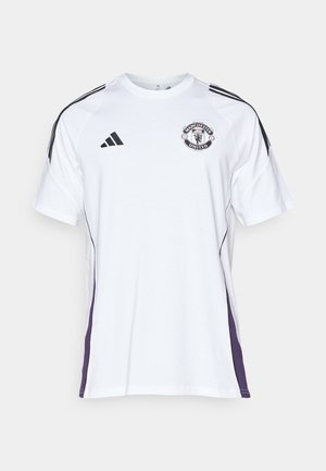 Fehér, rövid ujjú sportpóló fekete és lila oldalsó díszítésekkel, amelyen a Manchester United logója és három fekete csík látható a vállakon.