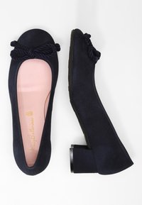 Navyblå mockabalettfutter som har en bågeaccent framtill, låg blockklack och en slät beige insida med guldbranding.