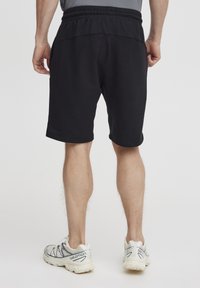 Schwarze Sportshorts aus weichem Stoff, mit einem elastischen Bund und leicht lockerer Passform, über dem Knie und ohne sichtbare Muster.