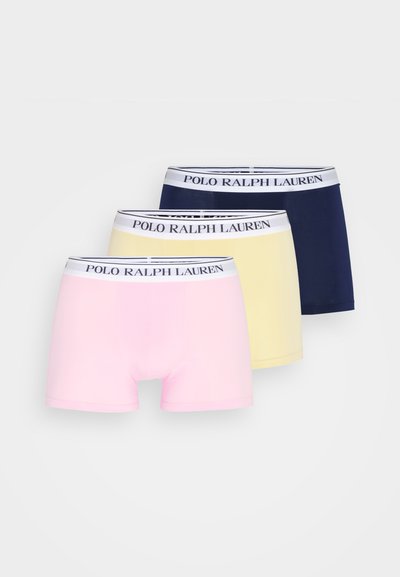 Três pares de boxers masculinos: rosa, amarelo e azul-marinho, com uma faixa branca apresentando "POLO RALPH LAUREN" em letras escuras.