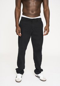 Sorte bomuldsbukser med lige ben-design, der har en knaplukning, bælteløkker og sidelommer. Parret med hvide sneakers.