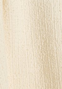 Miękka, teksturowana tkanina w jasnobeżowym kolorze z plecionym wzorem z podwyższonymi włóknami, tworząca subtelny kontrast w detalach powierzchni.