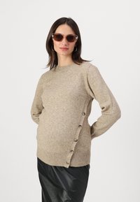 Beige neulepaita, jossa on pyöreä kaula-aukko, sivupainikkeet ja ribbireunus. Yhdistetty mustiin hameeseen ja aurinkolaseihin.