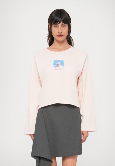 Sweat-shirt court rose clair à manches longues, avec un motif graphique d'un chien portant un nœud sur un fond bleu, associé à une jupe asymétrique gris foncé.